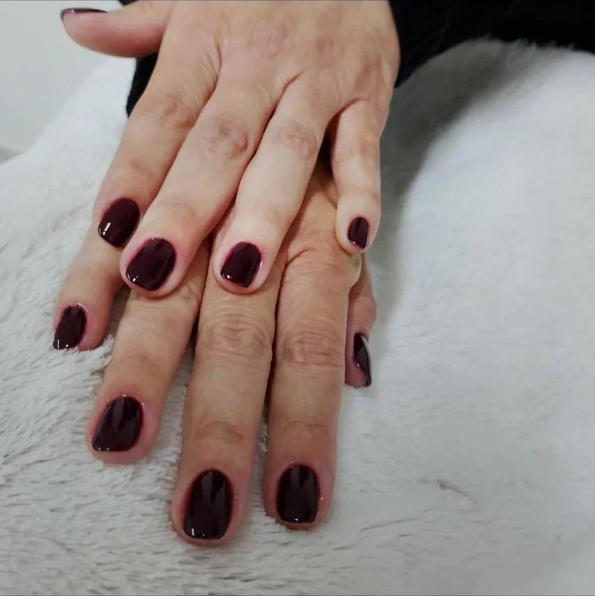 Mãos com unhas curtas esmaltadas em vinho escuro sobre uma manta clara