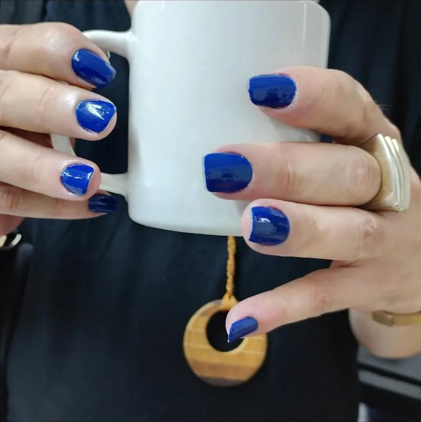 Mãos com unhas curtas azul royal segurando uma caneca branca